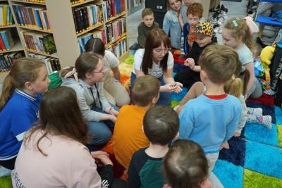 Owady dla odważnych. Gromada dzieci zainteresowanych owadami. Po środku dzieci prowadząca spotkanie pracownica Uniwersytetu Rozwoju.