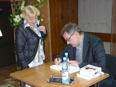 Artur Andrus wpisuje autografy  do książek zakupionych przez czytelników.