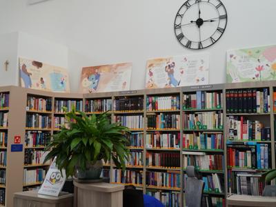Widok na wystawę ilustracji ustawioną na regałach bibliotecznych.
