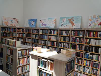 Widok na wystawę ilustracji ustawioną na regałach bibliotecznych.