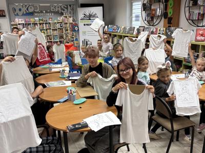 uczestnicy zajęć w bibliotece malują koszulki i torby