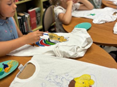 uczestnicy zajęć w bibliotece malują koszulki i torby