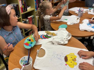 uczestnicy zajęć w bibliotece malują koszulki i torby