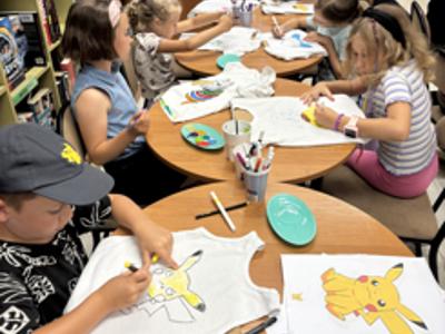 uczestnicy zajęć w bibliotece malują koszulki i torby