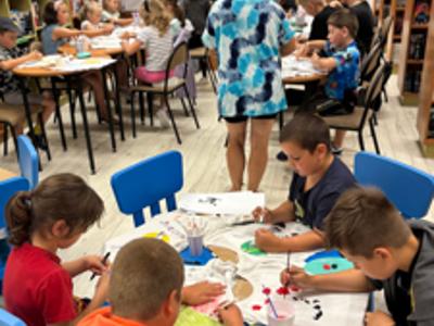 uczestnicy zajęć w bibliotece malują koszulki i torby