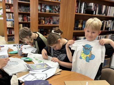 uczestnicy zajęć w bibliotece malują koszulki i torby