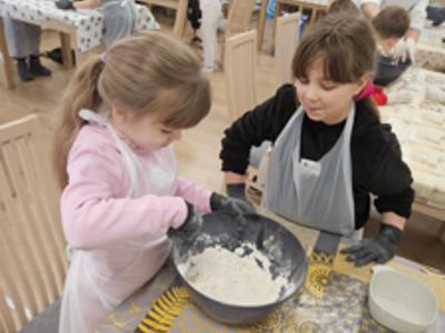 Dwie dziewczynki ugniatają ciasto na pizzę w misce 