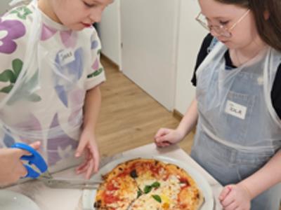 Dziewczynki kroją upieczoną pizzę specjalnymi nożyczkami