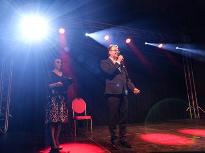 Na zdjęciu znajduje się Dyrektor Rakoniewickiego Ośrodka Kultury - Gizela Ziółkowska wraz z Zastępcą Burmistrza - Arkadiuszem Pawłowskim. Burmistrz wita przez mikrofon gości oraz składa życzenia Kobietom z okazji Dnia Kobiet. 