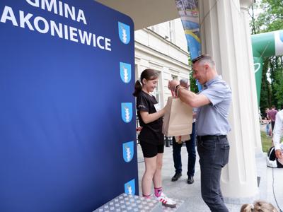 Dr Gerard Tomiak - burmistrz gm. Rakoniewice wręcza medal stojącej na podeście dziewczynce za zajęcie 3 miejsca w biegach