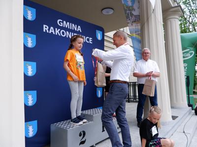 Krzysztof Krawczyk - przewodniczący Rady Miejskiej wręcza medal stojącej na podeście dziewczynce za zajęcie 2 miejsca w biegach. 