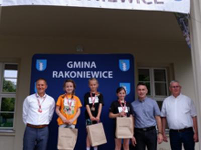 Zdjęcie grupowe dziewczyn na podium z Burmistrzem gm. Rakoniewice, Przewodniczącym oraz Zastępcą Przewodniczącego Rady Miejskiej.