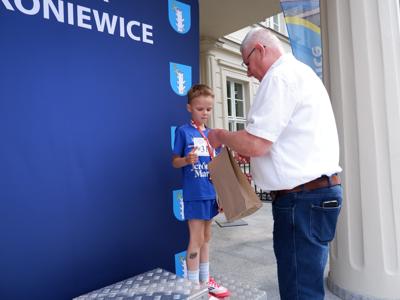 Marek Maćkowiak - zastępca przewodniczącego rady miejskiej wręcza nagrodę stojącemu na podeście chłopcu za zajęcie 3 miejsca w biegach.