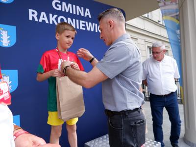Dr Gerard Tomiak - burmistrz gm. Rakoniewice wręcza medal stojącemu na podeście chłopcu za zajęcie 1 miejsca w biegach.