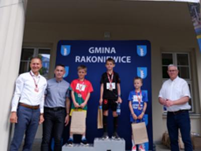 Zdjęcie grupowe chłopców na podium z Burmistrzem gm. Rakoniewice, Przewodniczącym oraz Zastępcą Przewodniczącego Rady Miejskiej.