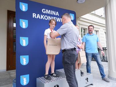 Dr Gerard Tomiak - burmistrz gm. Rakoniewice wręcza medal stojącej na podeście dziewczynce za zajęcie 2 miejsca w biegach. Obok stoi Arkadiusz Pawłowski