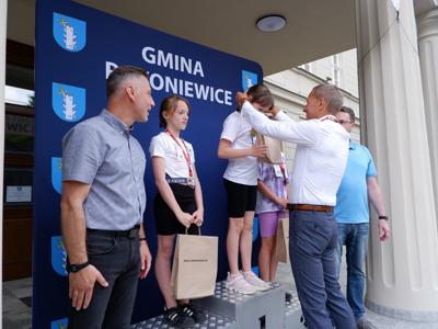 Krzysztof Krawczyk - przewodniczący Rady Miejskiej wręcza medal stojącemu na podeście chłopcu za zajęcie 1 miejsca w biegach. Obok stoi Burmistrz Rakoniewic