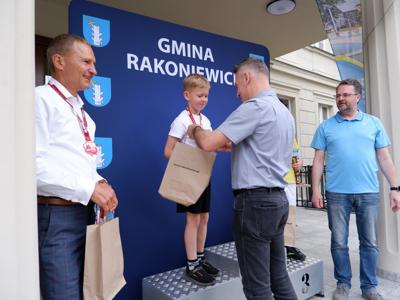 Dr Gerard Tomiak - burmistrz gm. Rakoniewice wręcza medal stojącemu na podeście chłopcu za zajęcie 2 miejsca w biegach. Obok stoi Krzysztof Krawczyk oraz Arkadiusz Pawłowski