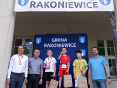 Zdjęcie grupowe chłopców na podium z Burmistrzem i Zastępcą Burmistrza gm. Rakoniewice oraz Przewodniczącym Rady Miejskiej.