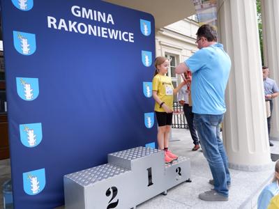 Arkadiusz Pawłowski - zastępca burmistrza gm. Rakoniewice wręcza medal stojącej na podeście dziewczynie za zajęcie 3 miejsca w biegach. 