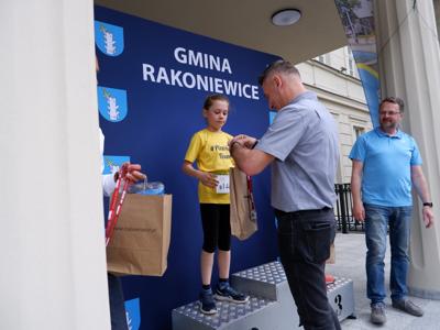 Dr Gerard Tomiak - burmistrz gm. Rakoniewice wręcza nagrodę stojącej na podeście dziewczynce za zajęcie 2 miejsca w biegach.