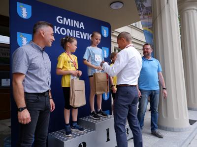 Krzysztof Krawczyk - przewodniczący Rady Miejskiej wręcza medal stojącej na podeście dziewczynie za zajęcie 1 miejsca w biegach.