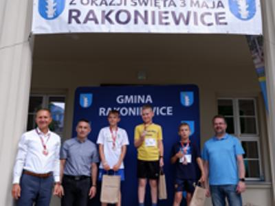Zdjęcie grupowe chłopców na podium z Burmistrzem i Zastępcą Burmistrza gm. Rakoniewice oraz Przewodniczącym Rady Miejskiej.