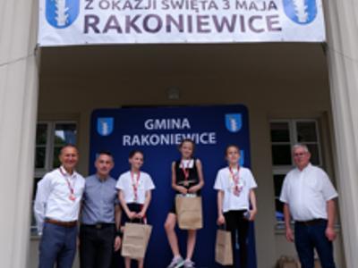 Zdjęcie grupowe dziewczyn na podium z Burmistrzem gm. Rakoniewice, Przewodniczącym oraz Zastępcą Przewodniczącego Rady Miejskiej.