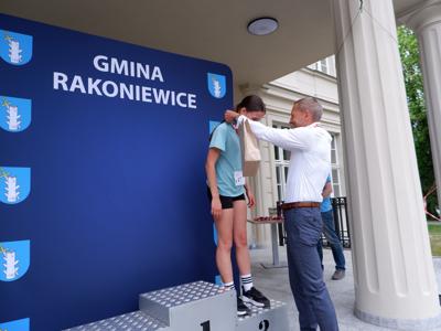 Krzysztof Krawczyk - przewodniczący Rady Miejskiej wręcza medal stojącej na podeście dziewczynie za zajęcie 3 miejsca w biegach.