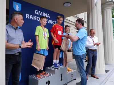 Arkadiusz Pawłowski - zastępca burmistrza gm. Rakoniewice wręcza medal stojącemu na podeście chłopcu za zajęcie 1 miejsca w biegach. 