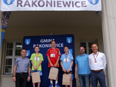 Zdjęcie grupowe chłopców na podium z Burmistrzem i Zastępcą Burmistrza gm. Rakoniewice oraz Przewodniczącym Rady Miejskiej.