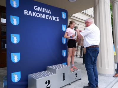 Marek Maćkowiak - zastępca przewodniczącego rady miejskiej wręcza medal stojącej na podeście dziewczynie za zajęcie 3 miejsca w biegach. 