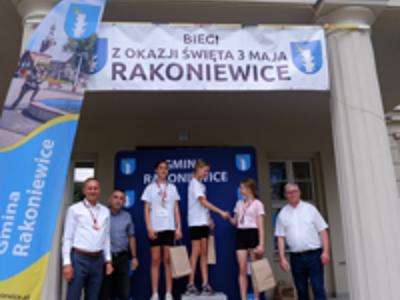 Zdjęcie grupowe dziewczyn na podium z Burmistrzem gm. Rakoniewice, Przewodniczącym oraz Zastępcą Przewodniczącego Rady Miejskiej.
