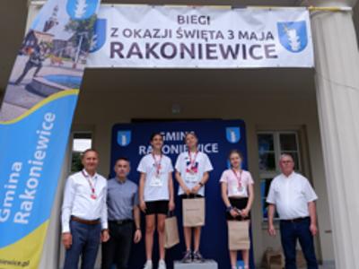 Zdjęcie grupowe dziewczyn na podium z Burmistrzem gm. Rakoniewice, Przewodniczącym oraz Zastępcą Przewodniczącego Rady Miejskiej.