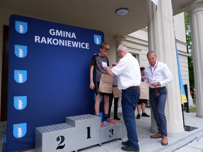 Marek Maćkowiak - zastępca przewodniczącego rady miejskiej wręcza nagrodę stojącemu na podeście chłopakowi za zajęcie 3 miejsca w biegach. 