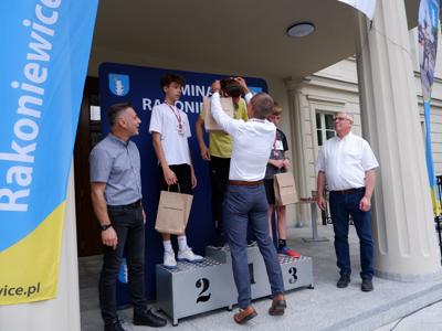 Krzysztof Krawczyk - przewodniczący Rady Miejskiej wręcza medal stojącemu na podeście chłopcu za zajęcie 1 miejsca w biegach.