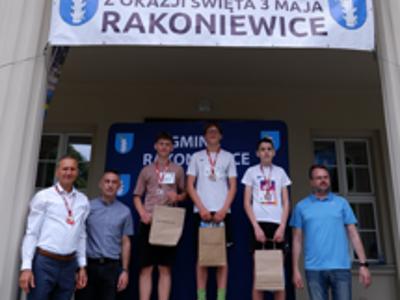 Zdjęcie grupowe chłopców na podium z Burmistrzem i Zastępcą Burmistrza gm. Rakoniewice oraz Przewodniczącym Rady Miejskiej.