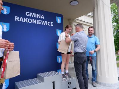 Dr Gerard Tomiak - burmistrz gm. Rakoniewice wręcza medal stojącej na podeście dziewczynie za zajęcie 3 miejsca w biegach.