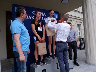 Krzysztof Krawczyk - przewodniczący Rady Miejskiej wręcza medal stojącej na podeście dziewczynie za zajęcie 1 miejsca w biegach.