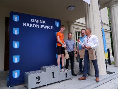 Krzysztof Krawczyk - przewodniczący Rady Miejskiej gratuluje stojącemu na podeście chłopcu za zajęcie 3 miejsca w biegach.