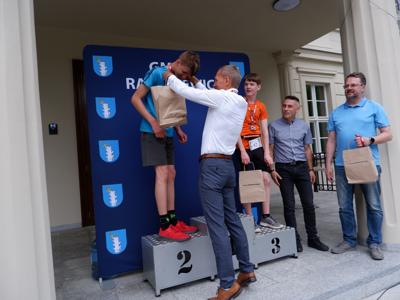 Krzysztof Krawczyk - przewodniczący Rady Miejskiej wręcza medal stojącemu na podeście chłopcu za zajęcie 2 miejsca w biegach.
