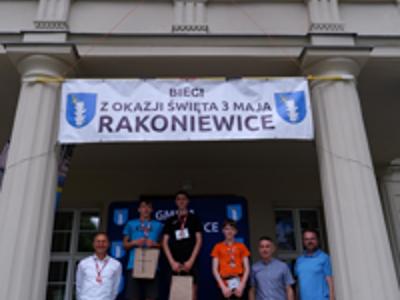 Zdjęcie grupowe chłopców na podium z Burmistrzem i Zastępcą Burmistrza gm. Rakoniewice oraz Przewodniczącym Rady Miejskiej.