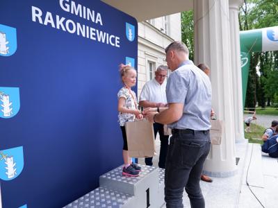 Dr Gerard Tomiak - burmistrz gm. Rakoniewice wręcza nagrodę stojącej na podeście dziewczynce za zajęcie 1 miejsca w biegach. 
