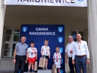Zdjęcie grupowe chłopców na podium z Burmistrzem gm. Rakoniewice, Przewodniczącym oraz Zastępcą Przewodniczącego Rady Miejskiej.