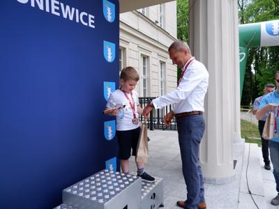 Krzysztof Krawczyk - przewodniczący Rady Miejskiej wręcza nagrodę stojącemu na podeście chłopcu za zajęcie 3 miejsca w biegach.