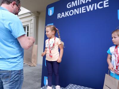 Arkadiusz Pawłowski - zastępca burmistrza gm. Rakoniewice wręcza nagrodę stojącej na podeście dziewczynce za zajęcie 2 miejsca w biegach. 