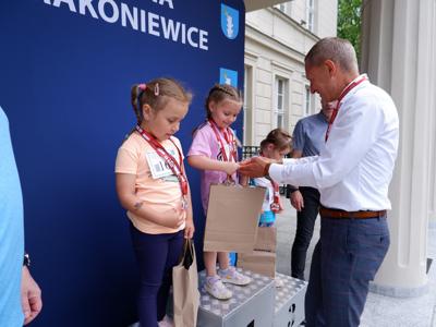 Krzysztof Krawczyk - przewodniczący Rady Miejskiej wręcza nagrodę stojącej na podeście dziewczynce za zajęcie 1 miejsca w biegach.