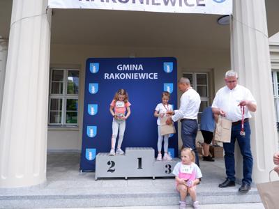 Krzysztof Krawczyk - przewodniczący Rady Miejskiej wręcza nagrodę stojącej na podeście dziewczynce za zajęcie 3 miejsca w biegach. Obok stoi zastępca przewodniczącego rady miejskiej Marek Maćkowiak