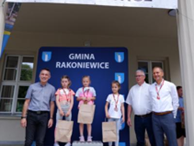 Zdjęcie grupowe dziewczyn na podium z Burmistrzem gm. Rakoniewice, Przewodniczącym oraz Zastępcą Przewodniczącego Rady Miejskiej.