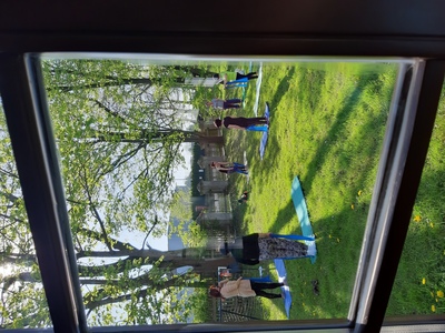 Zdjęcie kilku pań stojących na matach na trawie w trakcie ćwiczeń. Warsztaty pilates dla seniorów.